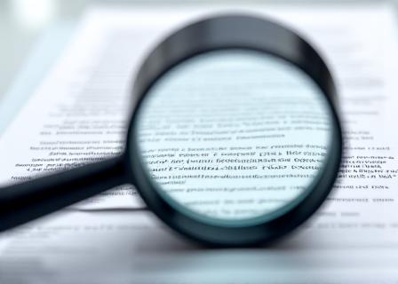 A magnifying glass hovering over complex legal fine print, highlighting the meticulous detail required for compliance.